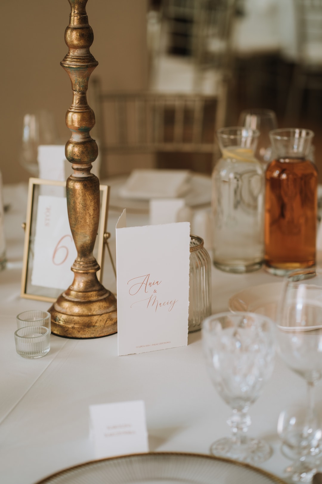 Elegancka aranżacja stołu weselnego ze złotym świecznikiem, kartą dla gościa, szklankami i dekoracją w jasnej palecie