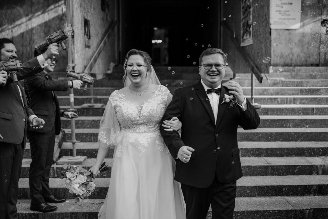 Para Młoda schodzi po schodach podczas ceremonii ślubnej, gość z balonów mydlanych, bukiet ślubny widoczny w kadrze.