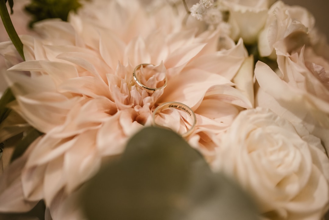 Złote obrączki ślubne na delikatnych kwiatach w jasnej palecie, kompozycja kwiatowa na stół w tonach kremowych i różu.