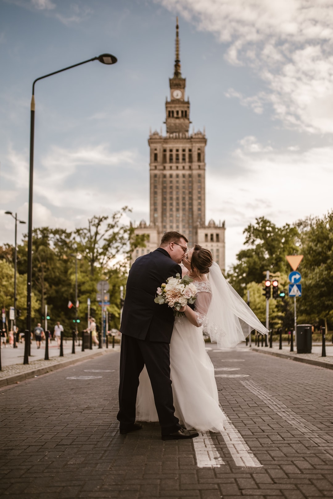 Para Młoda w strojach ślubnych na tle Pałacu Kultury, panna młoda z bukietem ślubnym, ulica z zielenią