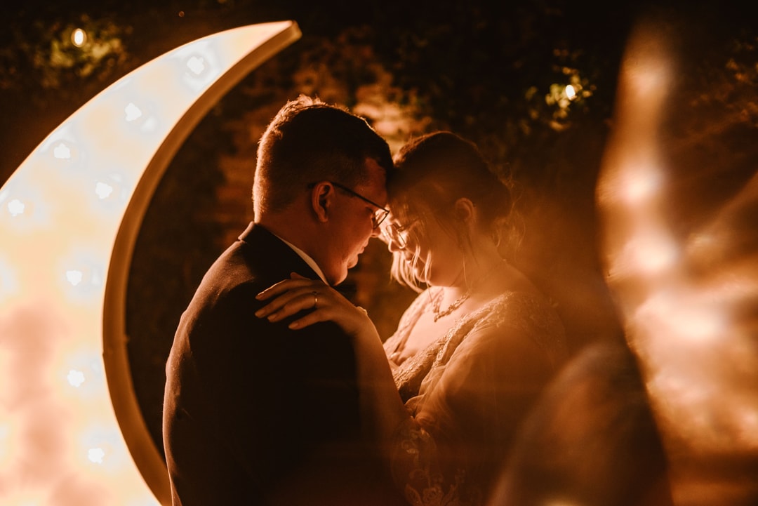 Para podczas tańca przy dekoracji z podświetlanym łukiem kwiatowym, ciepłe oświetlenie, romantyczna atmosfera.