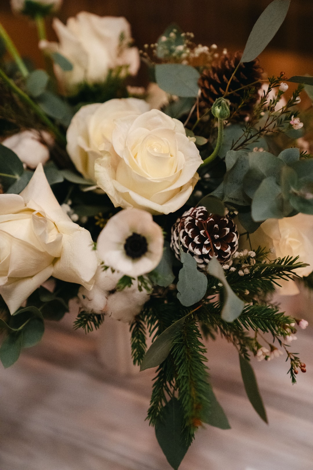 Kompozycja kwiatowa na stół z białymi różami, jasną zielenią eukaliptusa, suszonym kwiatem oraz delikatnymi drobnymi kwiatkami w pastelowych tonach.