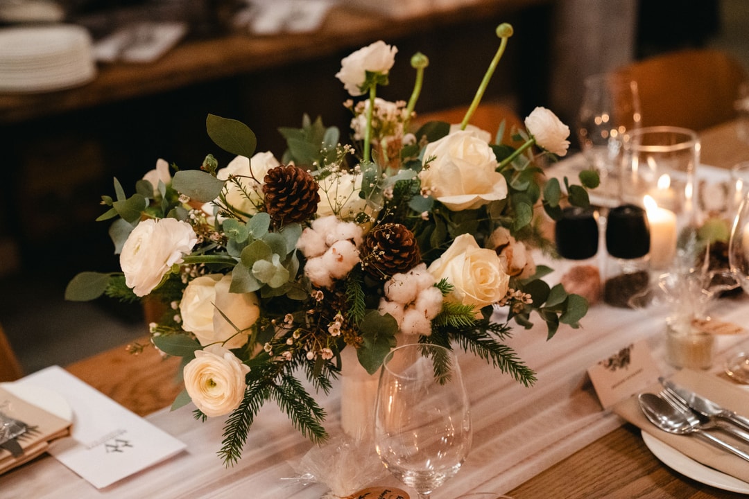 Kompozycja kwiatowa na stół ze świeżymi kwiatami w jasnej palecie, zielenią i naturalnymi elementami na drewnianym blacie