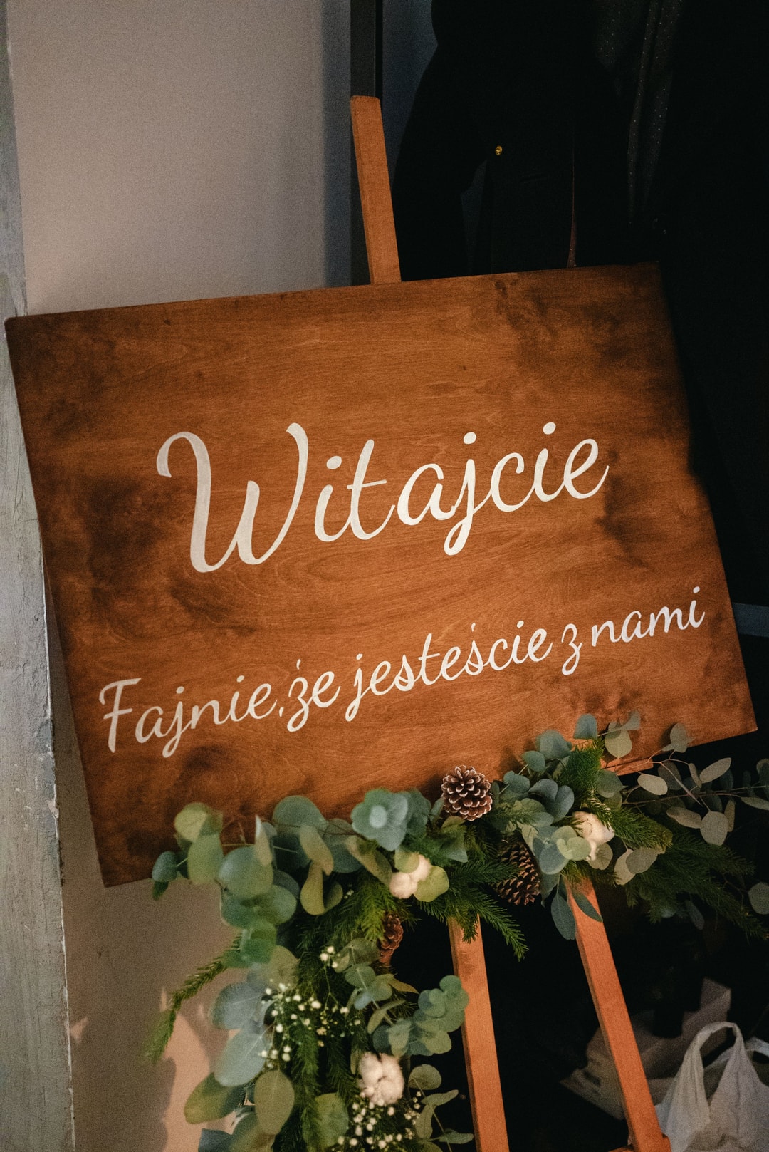 Drewniana tablica z napisem witajcie i dekoracja stołu, girlanda z zielenią, kwiatami i szyszkami