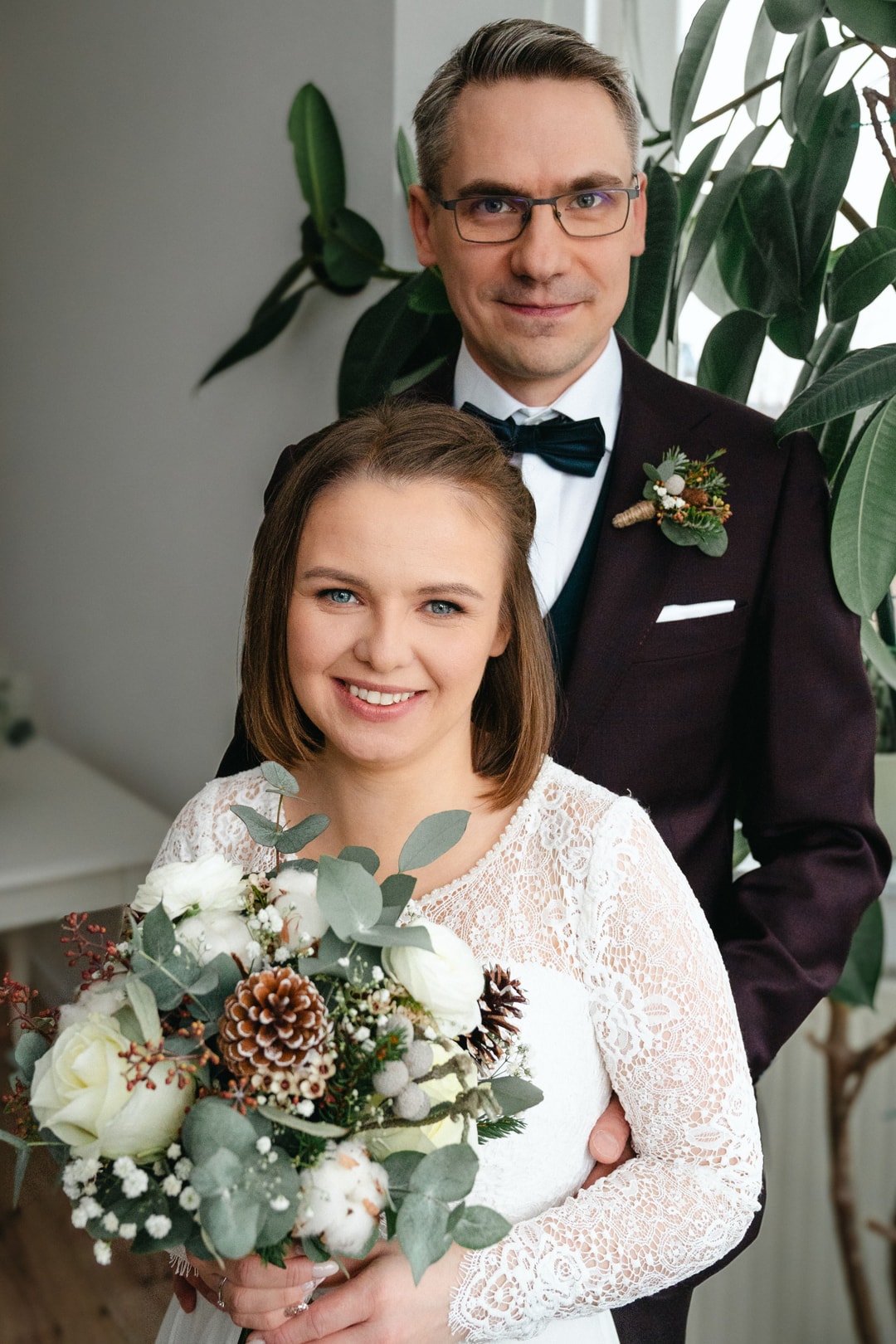 Para Młoda pozuje do zdjęcia - kobieta z bukietem ślubnym z białymi kwiatami, zielenią i brązowymi detalami, mężczyzna w czarnym garniturze z butonierką.