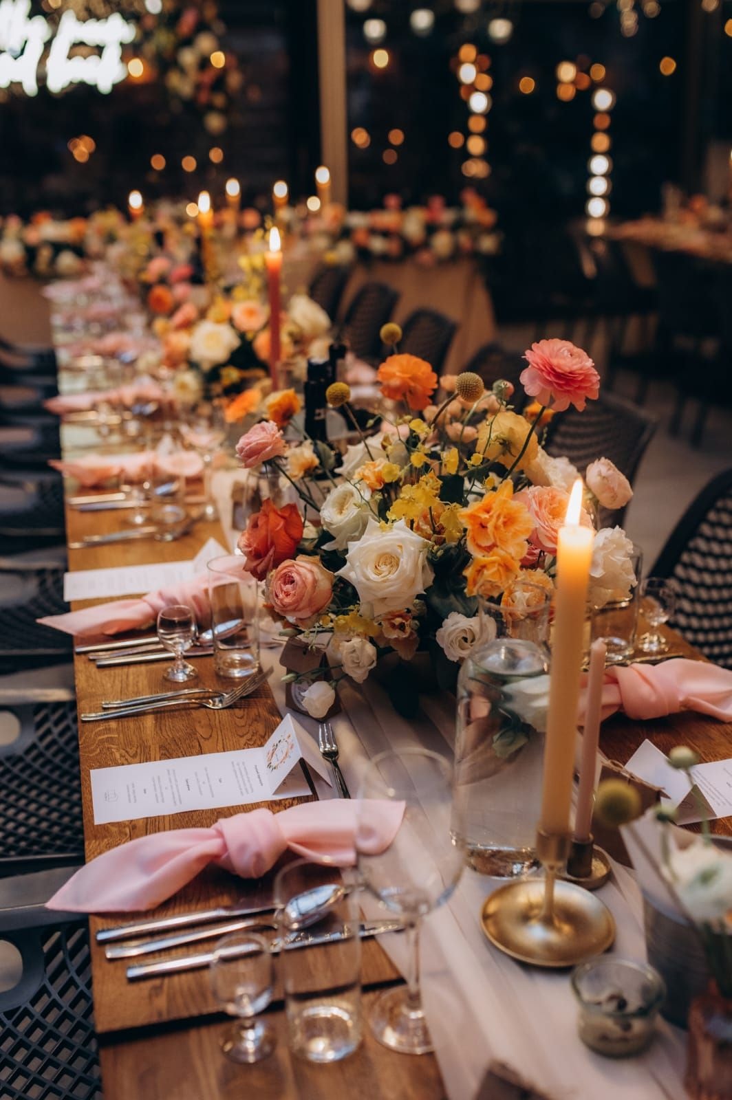Aranżacja stołów weselnych z kompozycjami kwiatowymi w różowych, pomarańczowych i kremowych tonach, świecami i dekoracją sali