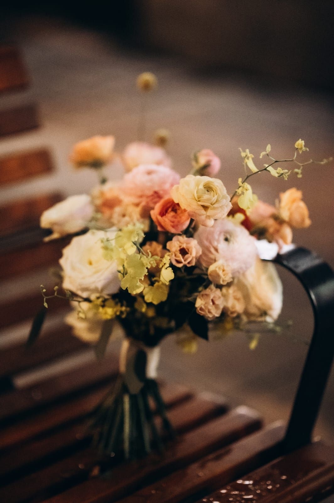 Bukiet ślubny z różami w jasnej palecie, kwiatami sezonowymi i zielenią, na drewnianym tle