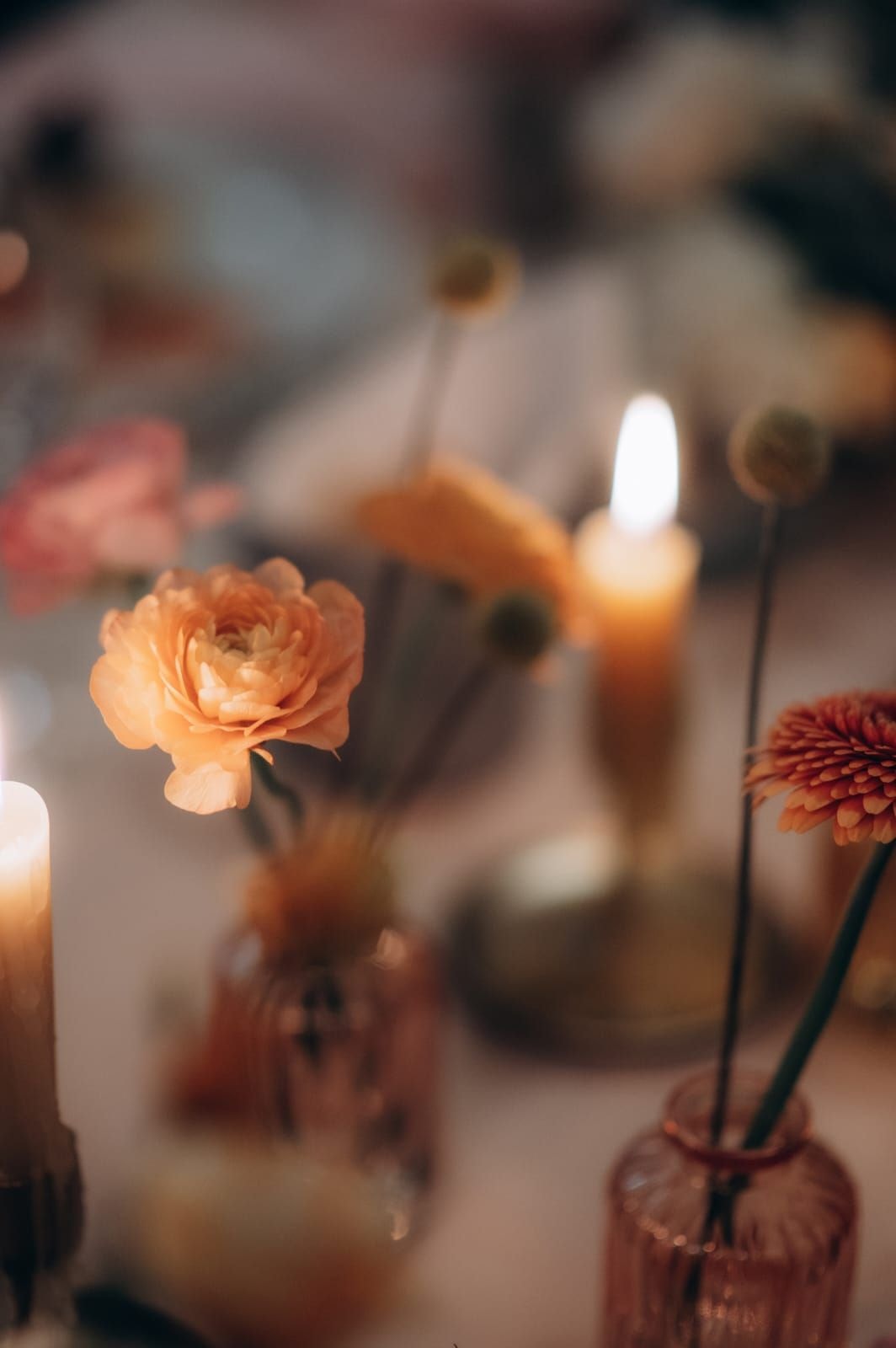 Kompozycja kwiatowa na stół z pomarańczową różą, czerwoną daliią i płonącymi świecami w tle