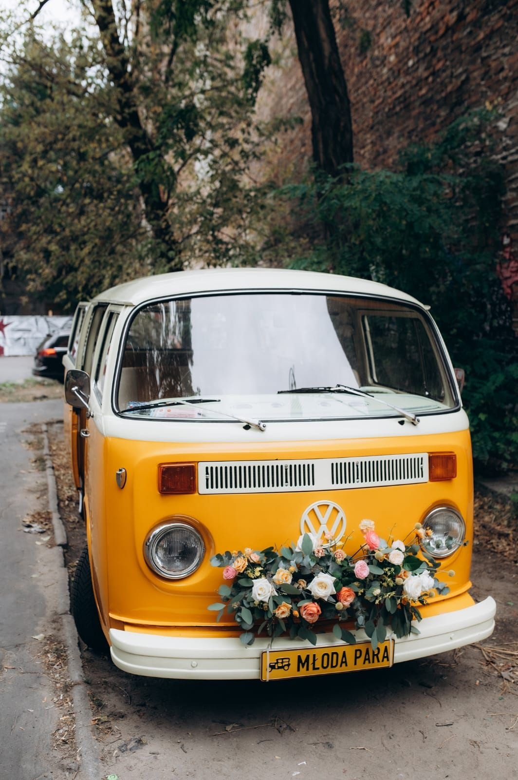 Żółty autobus Volkswagen z białym dachem, ozdobiony kompozycją kwiatową na przednią część, rejestracja MŁODA PARA
