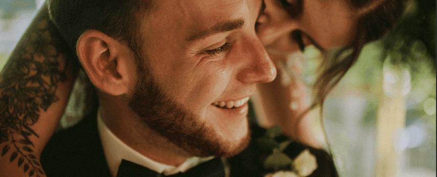 Mężczyzna w garniturze uśmiechający się podczas ceremonii ślubnej, dekoracja kwiatowa bukiet ślubny widoczna w tle