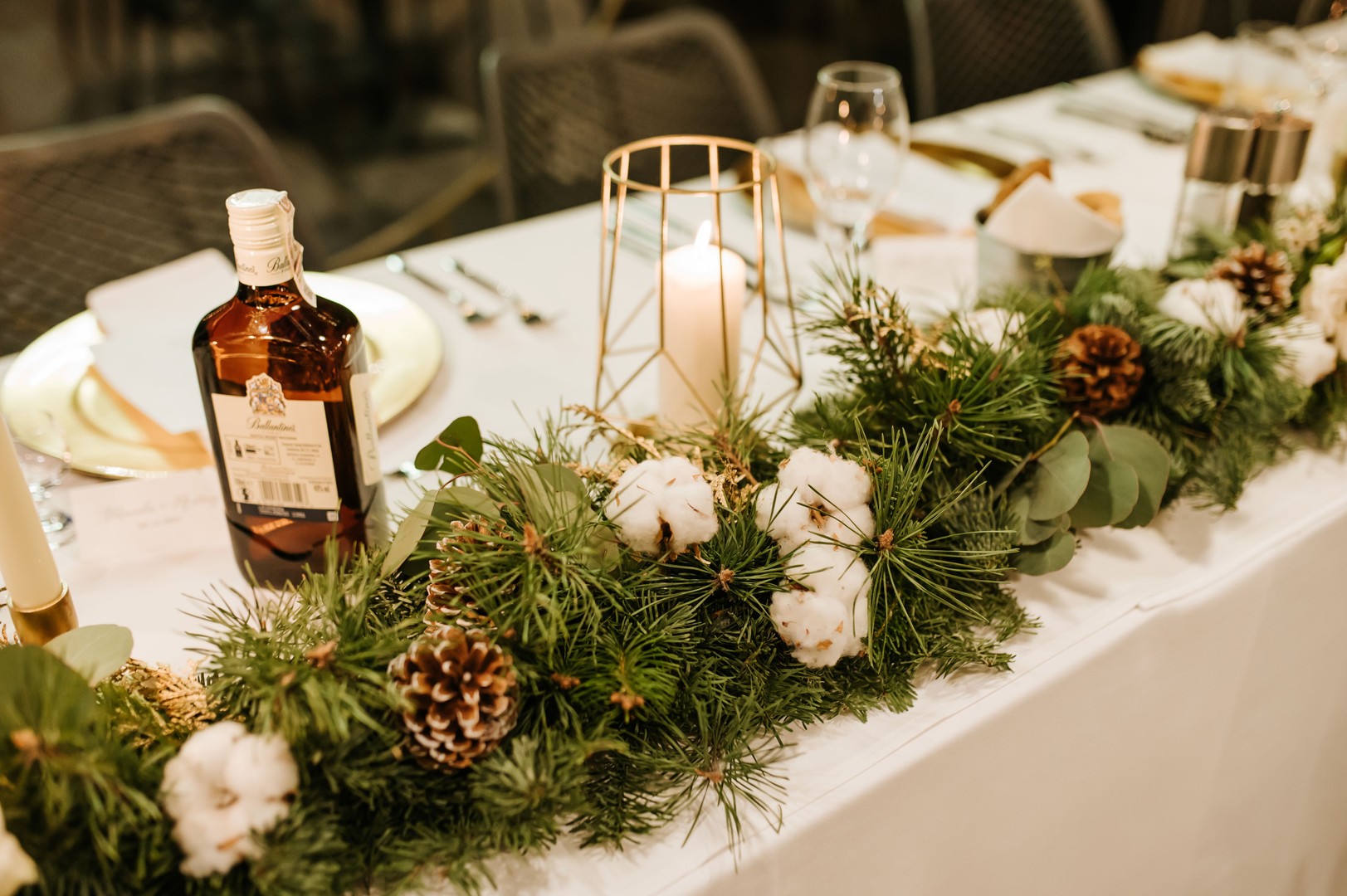 Dekoracja stołu prezydialnego na ślub zimowy z szyszkami oraz bawełną. W tle złoty lampion ze świecą
